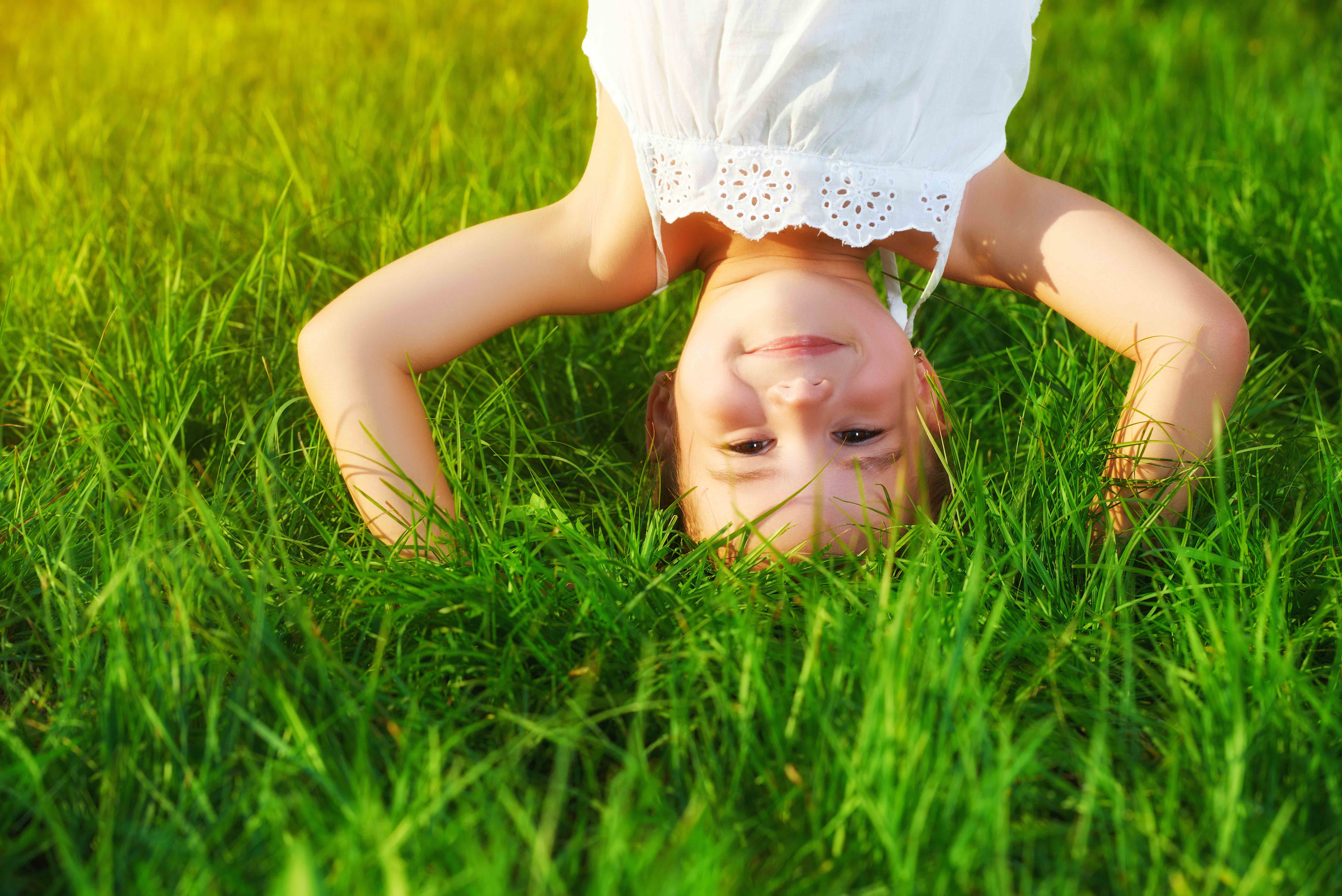 happy child girl standing upside down on his head on the grass in the summer